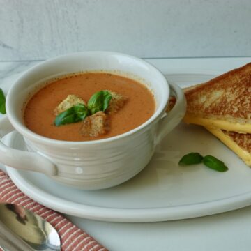 Tomato soup with basil served in a bowl with grilled cheese on the side.
