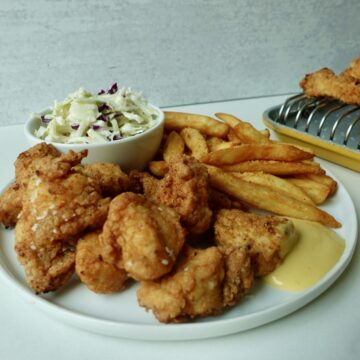 Large batch crispy chicken nuggets with fries and coleslaw on a plate