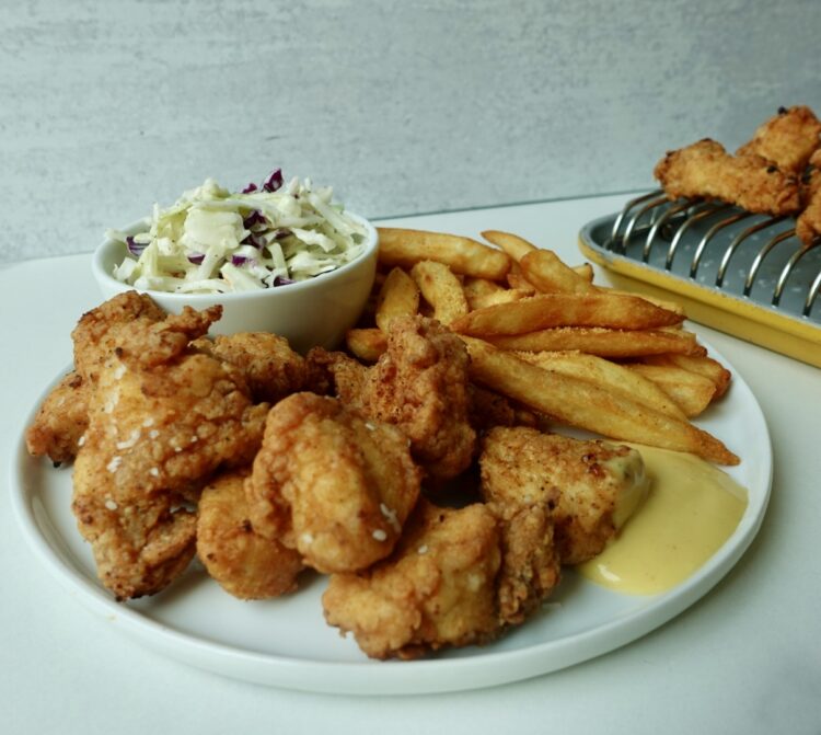 Large batch crispy chicken nuggets with fries and coleslaw on a plate