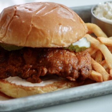 Crispy Nashville hot chicken sandwich on a toasted brioche bun with spicy ranch sauce, dill pickles, and French fries.