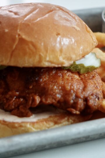 Crispy Nashville hot chicken sandwich on a toasted brioche bun with spicy ranch sauce, dill pickles, and French fries.