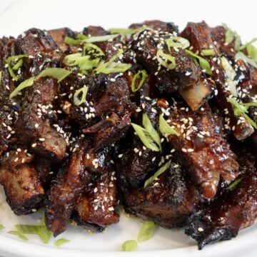 Fall-off-the-bone sticky Asian ribs glazed with a sweet and savory hoisin sauce and garnished with sesame seeds and green onions.