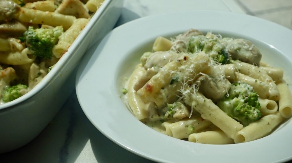 creamy chicken and broccoli ziti topped with melted mozzarella cheese in a baking dish.