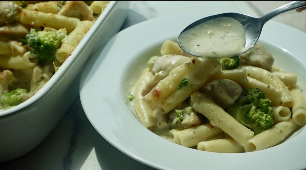creamy chicken and broccoli ziti topped with melted mozzarella cheese in a baking dish.