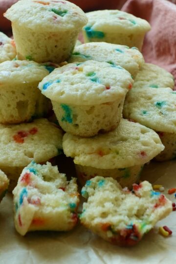 Homemade party cake mini muffins filled with rainbow sprinkles, with one muffin split open to show its soft, moist crumb.